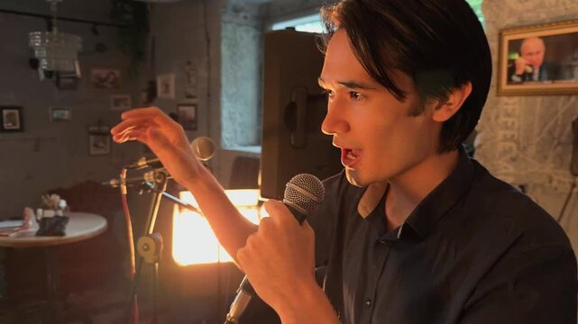 Expressive Asian Male Author Performing Poetry Slam Monologue Into Microphone On Cozy Cafe Stage With Warm Backlight During Intimate Literature Storytelling Evening Close Up Authentic Handheld Shot
