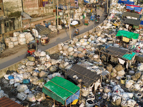 Aerial view of Buriganga river canal, featuring piles of plastic waste and recycling materials in large sacks along the banks, with local traffic in Dhaka, Dhaka Division, Bangladesh.