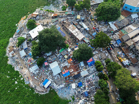 Aerial view of the Buriganga river canal area featuring dense clusters of white storage bags, scattered buildings, and trees along the waterfront in Dhaka, Dhaka Division, Bangladesh.