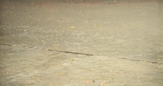 Cinematic detailed shot of heavy monsoon raindrops hitting, splashing, and forming ripples on a wet floor surface in Guwahati, Assam, India