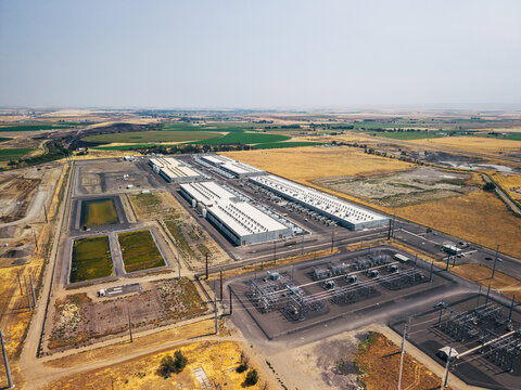 Aerial view of a large data center complex with extensive server buildings and an adjacent electrical substation, situated in a dry, rural landscape in Umatilla, Oregon, United States.