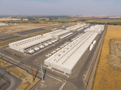 Aerial view of a large industrial data center complex with long white buildings and rooftop HVAC units surrounded by dry fields in Hermiston, Oregon, United States.