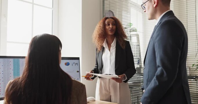 Team meeting in office for strategy discussion. Confident manager presents report to colleagues by monitor with charts, driving analysis and planning. Business teamwork enables sound decisions.