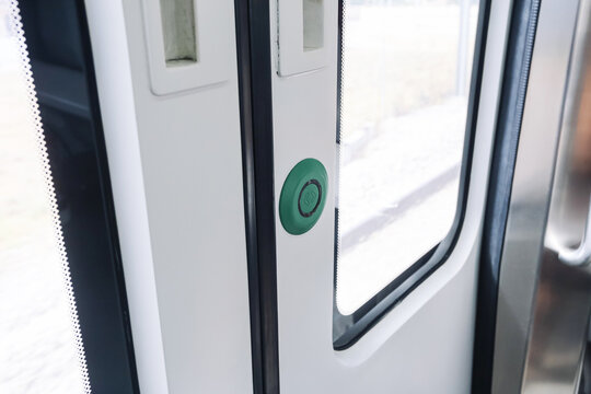 Green door request button beside train window in public transport interior. Passenger access control detail with white panel glass frame modern railway carriage travel and transit background.