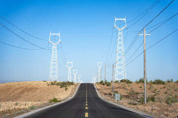 Naklejka premium high voltage transmission towers lining a straight road in the arid desert landscape under blue sky