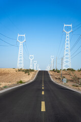Naklejka premium High voltage transmission towers along a paved road under blue sky