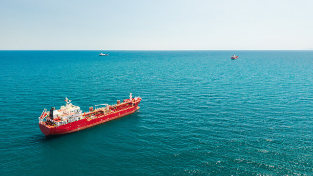 Red tanker ship anchored in turquoise sea viewed from aerial drone