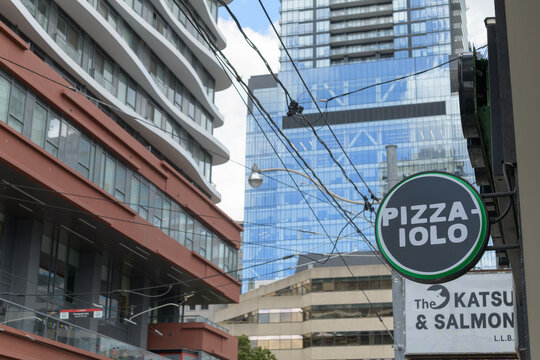 exterior building facades and wall-mounted round projecting sign outside entrance to Pizzaiolo, a casual eatery, located here at 289 Dundas St W, Toronto