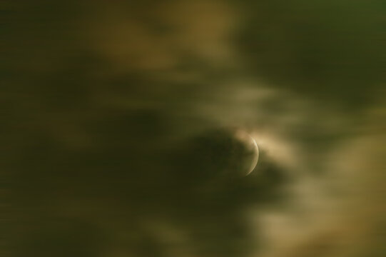 View of the lunar eclipse blood moon partially obscured by dark, moody clouds in the night sky over Jahanian, Pakistan.