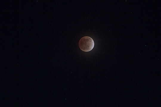 View of a lunar eclipse appearing as a reddish moon against the dark night sky with visible stars in Jahanian, Pakistan.