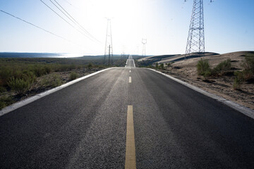 Naklejka premium straight asphalt road stretching through desert landscape with electricity towers