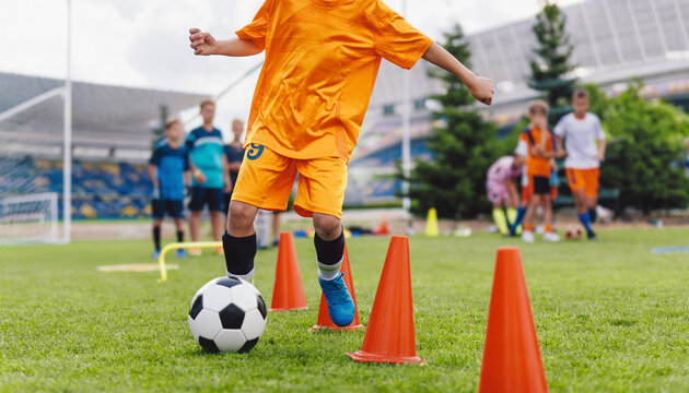 Junior Soccer Player in Orange Uniform Dribbling Ball Through Agility Cones - Youth Football Stadium Skill Training Practice