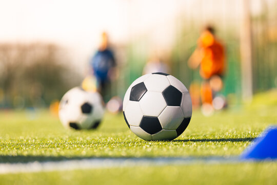Close-Up of Soccer Ball Resting on Green Grass Pitch with Blurred Players in Background - Youth Football Practice Equipment Concept
