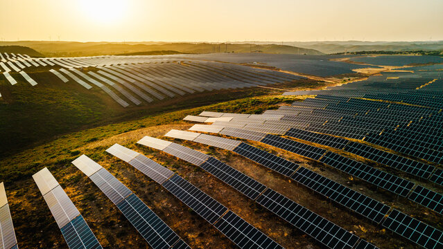 Aerial view of extensive photovoltaic panel arrays covering rolling rural hills in warm golden evening light.