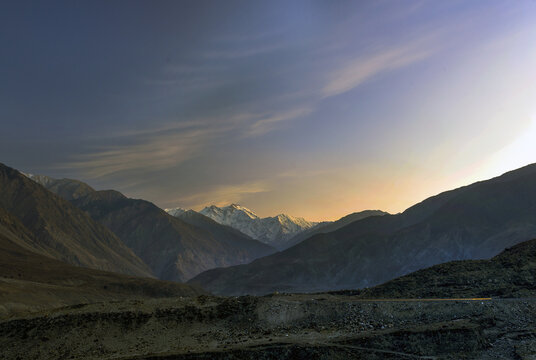 View of the snow-capped peak of Nanga Parbat illuminated by the golden hour light above rugged mountain slopes and a rocky landscape in Pakistan.