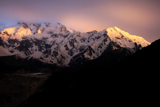View of Nanga Parbat illuminated by the golden light of sunset with snow-covered peaks and dramatic shadows in Pakistan.