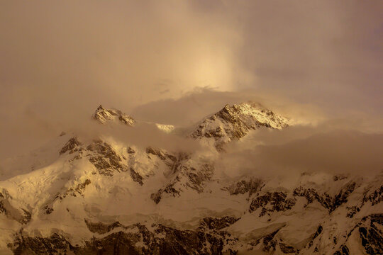 View of Nanga Parbat with snow-capped peaks partially obscured by clouds during the golden hour in Pakistan.