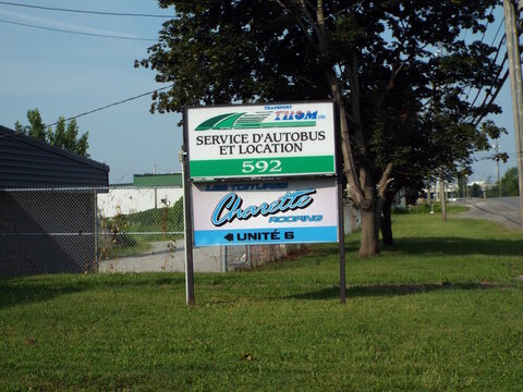 Gatineau, Quebec, Canada &ndash; July 02, 2026: An outdoor business sign reads "Service D'Autobus Et Location 592" alongside a "Charette Roofing" unit label on Rue de B&eacute;cancour.