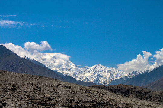 View of the snow-capped peaks of Nanga Parbat rising above rocky terrain under a clear blue sky in Chilas, Pakistan.