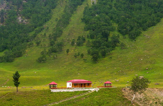 View of a small building with a red roof nestled in the lush green slopes of the mountains near Burzil Pass in Astore, Gilgit Baltistan, Pakistan.