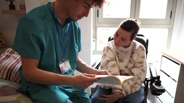 Compassionate male nurse providing care and companionship by reading a book aloud to a smiling woman with a disability sitting in a modern electric wheelchair in a brightly lit room