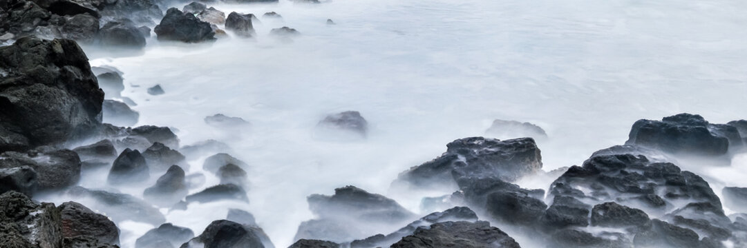 View of dark volcanic rocks surrounded by white sea foam and crashing waves along the rugged coastline of Easter Island, Valparaiso, Chile.