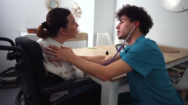 Compassionate male nurse providing home care, using a stethoscope to listen to the breathing of a female patient sitting in a wheelchair during a regular medical check up at her residence