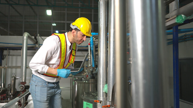 Engineer using laptop to monitor chia seed fruit juice production machinery in automated beverage factory system