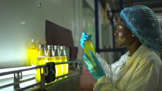 Quality control worker examining chia seed fruit juice bottles under light on conveyor belt