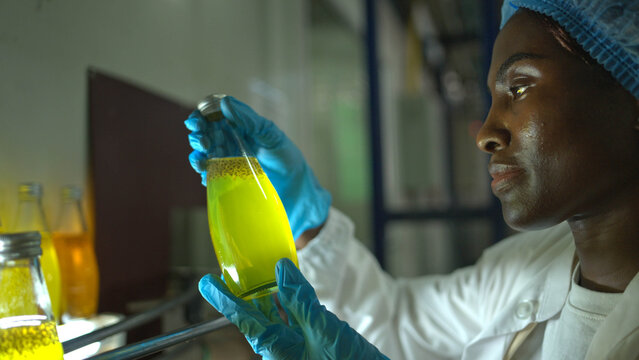 Quality control worker examining chia seed fruit juice bottles under light on conveyor belt