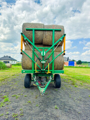 Farm vehicle transporting hay bales on a rural road under a cloudy sky during daytime © DSMT