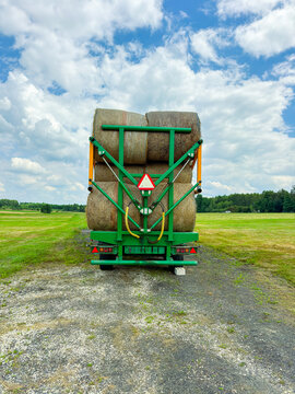 Truck carries large bales of hay on a field under a blue sky with clouds during daytime in a rural area