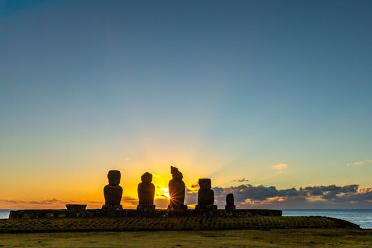 View of Moai statues standing on stone platforms overlooking the Pacific Ocean in a grassy coastal landscape on Easter Island, Valparaiso, Chile. Moais Tahai Archaeological Complex.