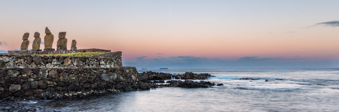 Moais Tahai Archaeological Complex. View of the iconic Moai statues standing on a historic stone platform overlooking the calm ocean at sunset in Easter Island, Valparaiso, Chile.