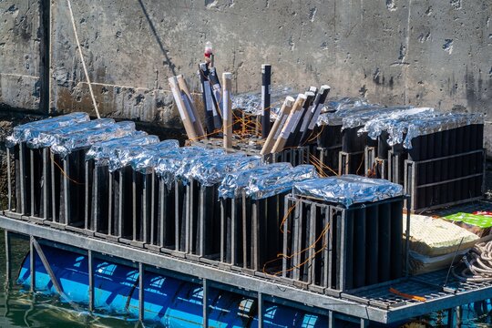 View of fireworks launch tubes arranged in metal racks on a floating platform with blue barrels against a concrete wall in Cascais, Lisbon, Portugal.