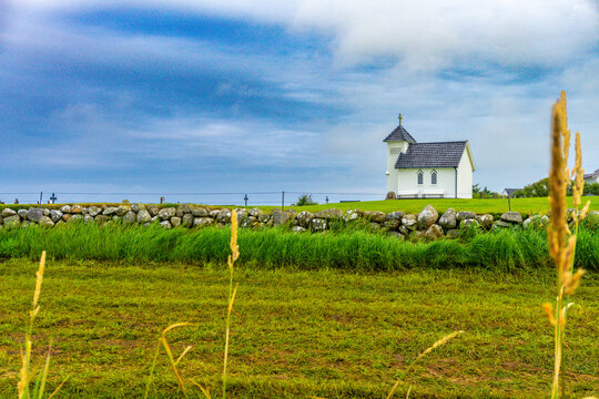 Small white chapel at Varhaug gamle kirkeg&aring;rd in Norway, surrounded by a green cemetery landscape under a dramatic deep blue sky.