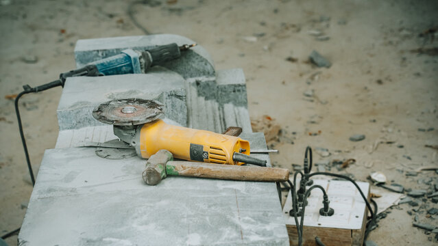 View of stone carving tools including an angle grinder and hammer resting on a large block of grey stone in a workshop in India.