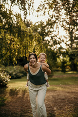 Naklejka premium Mother giving piggyback ride to child in summer park