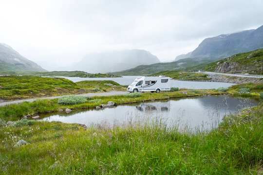 White Motorhome Parked Near Mountain Lake. A white camper van sits on a roadside patch overlooking a serene lake and misty hills in a remote highland area.