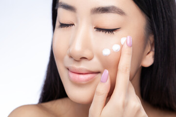 Beauty portrait of calm woman with closed eyes touching cream on cheek with her finger while...