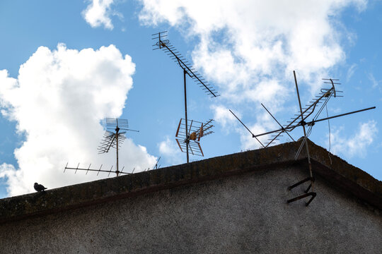 View of television antennas mounted on a rooftop with a small bird perched on the edge against a blue sky with clouds in Coimbra, Coimbra, Portugal.