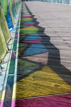 View of the colorful glass panels of the Ponte Pedonal Pedro e Ines casting vibrant geometric shadows onto the wooden walkway in Coimbra, Coimbra, Portugal.