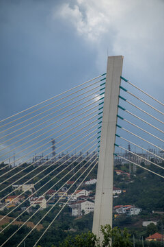 View of the concrete pylon and steel cables of the Rainha Santa Isabel Bridge rising above the hillside houses and lush greenery in Coimbra, Coimbra, Portugal.