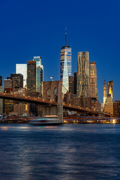 Scenic view of the downtown Manhattan skyline at dawn showcasing the illuminated Brooklyn Bridge and financial district skyscrapers along the East River in New York.