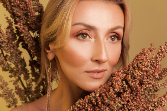 Close up portrait of attractive woman with golden makeup posing with dried flowers isolated on yellow background