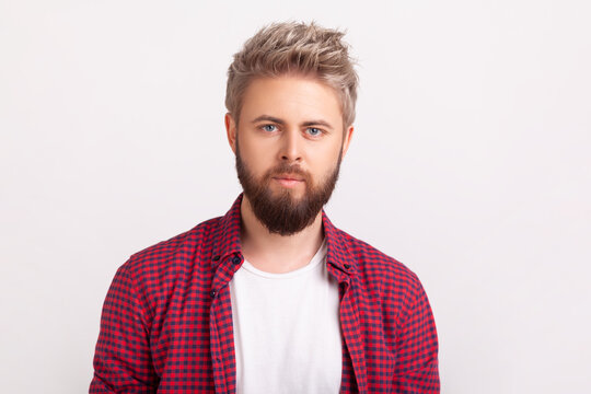 Confident bearded man with neutral expression looking at camera with calm and steady gaze posing isolated over white background