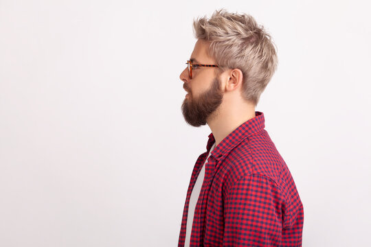 Bearded man in eyeglasses in profile position looking to side with serious facial expression posing isolated over white background
