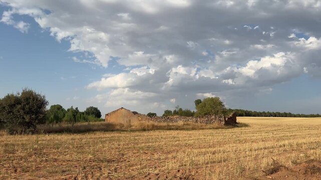 Dramatic clouds floating over a rural landscape with an abandoned building in a mowed grain field. Beautiful and peaceful countryside view