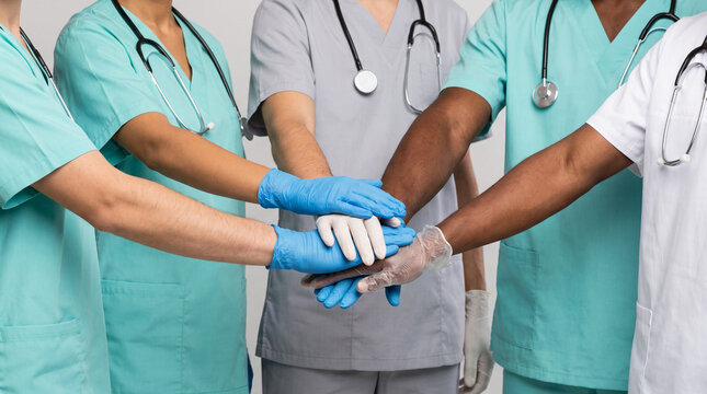 Diverse medical team in scrubs stacking gloved hands together, showing unity and teamwork