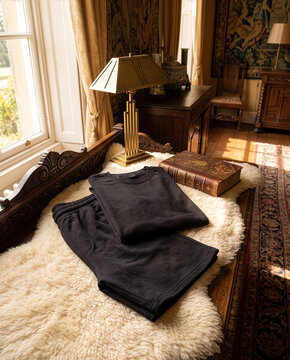 Folded blank black t-shirt and shorts set mockup on sheepskin rug placed on antique wooden daybed in luxury classic interior
